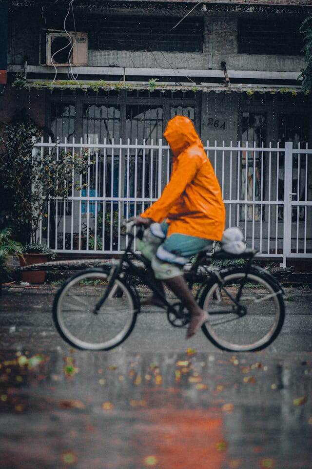 Person riding a bike through a wet street in an orange raincoat- raincoats made from GORE-TEX contain PFAS